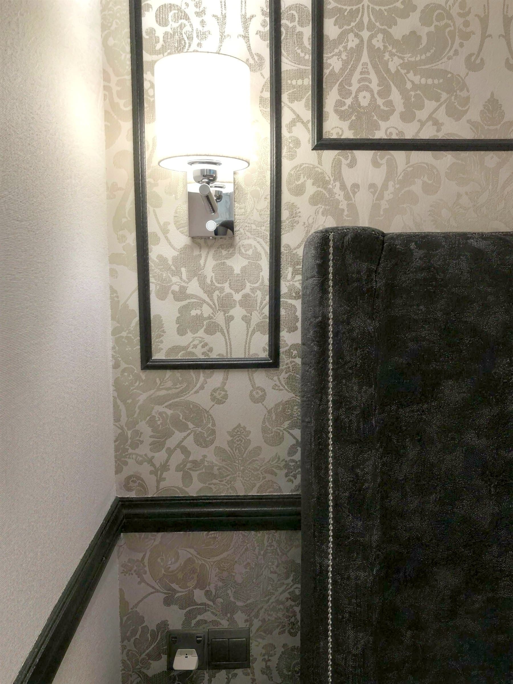 Channel-tufted headboard detail with wall sconce and damask paper